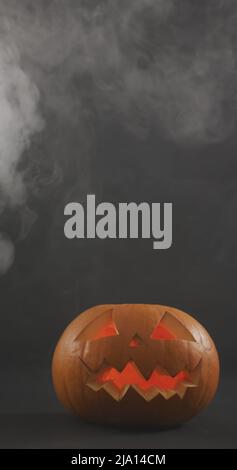 Immagine verticale di zucche di Halloween scolpite illuminate con nuvole di fumo su sfondo grigio Foto Stock