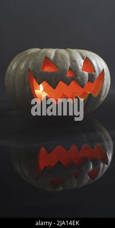 Immagine verticale di chiusura della zucca di Halloween scolpita illuminata su sfondo grigio Foto Stock