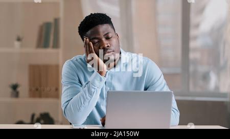 Sonnolenta uomo africano giovane uomo maschio investitore imprenditore napping alla scrivania ufficio improvvisamente svegliarsi scioccato confuso americano tipo risposta chiamata in arrivo Foto Stock
