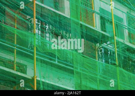 Rete protettiva per facciate per ponteggi, la griglia dell'edificio copre la facciata di un vecchio edificio storico chiuso per ristrutturazione. Cantiere. Foto Stock