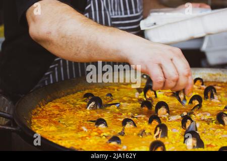 Uno chef professionista prepara la paella, un piatto tradizionale spagnolo di riso con cozze, in un enorme calderone. Una classica paella spagnola con frutti di mare. Stree Foto Stock