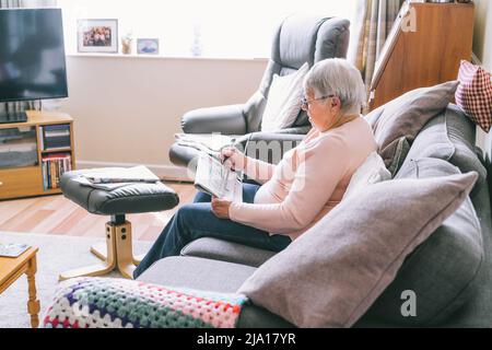 Donna anziana, 80s adulti, nonna, facendo cruciverba puzzle nel suo soggiorno seduto sul divano. Hobby di pensionamento per la memoria di addestramento. Alzhe Foto Stock