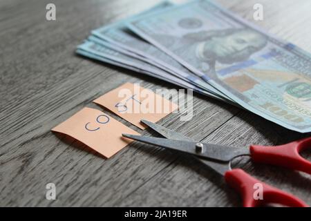 Forbici, denaro e nota con costo del testo. Concetto finanziario, riduzione dei costi, riduzione delle spese Foto Stock