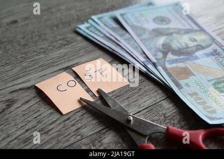 Forbici, denaro e nota con costo del testo. Concetto finanziario, riduzione dei costi, riduzione delle spese Foto Stock