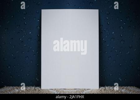 Un foglio bianco di carta si trova in posizione verticale su un tappeto chiaro e su uno sfondo isolato e scuro con gocce d'acqua Foto Stock