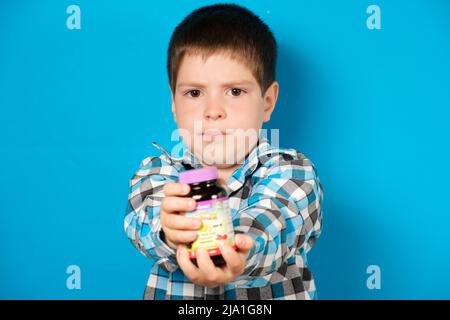 Un ragazzo di 4 anni tiene in mano un vasetto di vitamina D o altri integratori alimentari su sfondo blu. 22 maggio 2022, Zaporozhye, Ucraina. Foto Stock