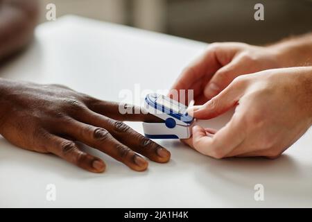 Primo piano di un medico irriconoscibile che applica il pulsossimetro al dito nero dei pazienti durante l'appuntamento Foto Stock