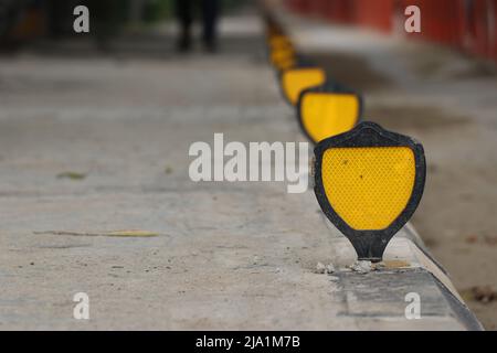 Catarifrangente stradale giallo sul lato della strada in una vista in linea Foto Stock