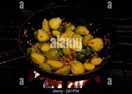 bruxelles germogli cottura con pancetta di manzo e burro in una padella calda al fuoco Foto Stock