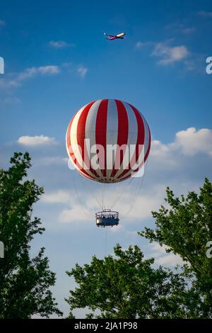 Budapest, Ungheria - Apr 30 2022: Aereo che vola sopra il mongolfiera incorniciata da alberi a Budapest Városliget (parco cittadino) Foto Stock