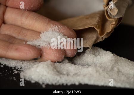 Sale di roccia in primo piano sparso su uno sfondo nero e la mano di una donna, sale e spezie Foto Stock