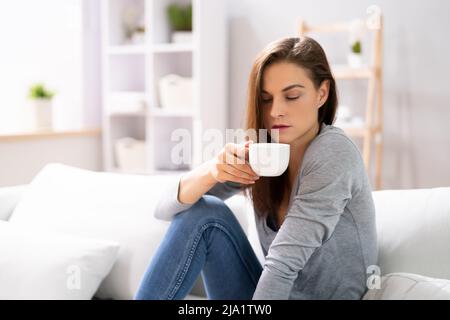 Donna seduta sul divano a casa con tazza caffè Foto Stock