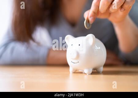 Mano della donna che inserisce il coin in Piggybank sopra la scrivania di legno Foto Stock