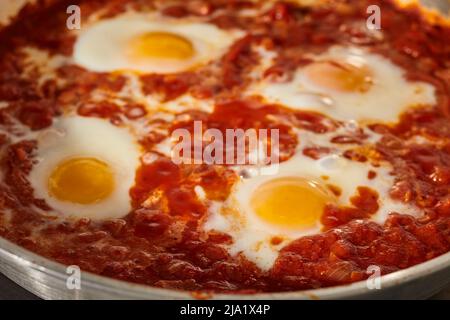 Shakshuka, il piatto israeliano di salsa di pomodoro e uova, cucinando in una padella d'acciaio. Foto Stock