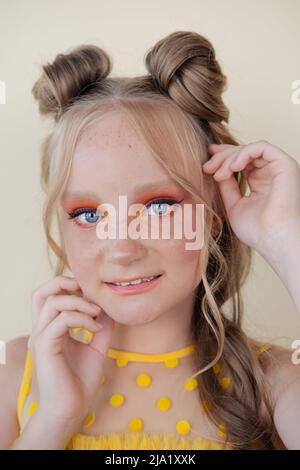 affascinante ragazza bionda tween con trucco arancione su sfondo giallo. ritratto adolescente. Foto Stock