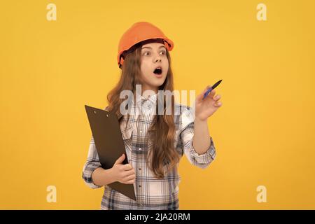 scioccata ragazza teen in casco e camicia a scacchi facendo appunti sulla clipboard, lavorando Foto Stock