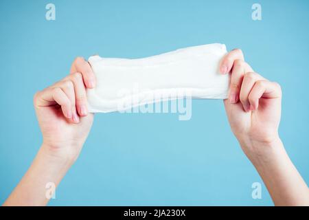 assorbente igienico bianco nelle mani di una ragazza su sfondo blu Foto Stock