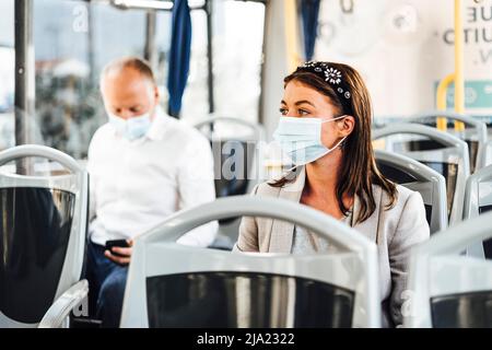 Viaggiatori che indossano maschere protettive che viaggiano con autobus pubblico Foto Stock