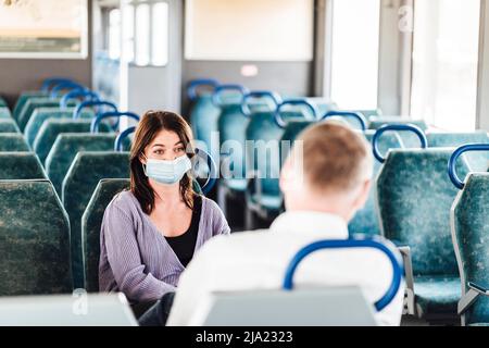 Un paio di amici che indossano la maschera e parlano bene mentre si viaggia in treno Foto Stock