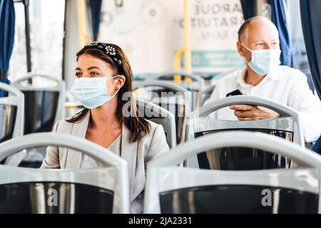 Viaggiatori che indossano maschere protettive che viaggiano con autobus pubblico Foto Stock