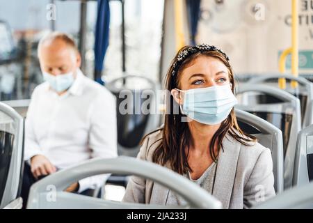 Viaggiatori che indossano maschere protettive che viaggiano con autobus pubblico Foto Stock
