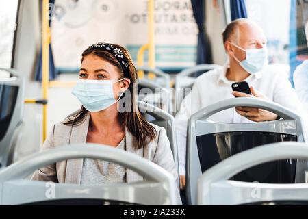 Viaggiatori che indossano maschere protettive che viaggiano con autobus pubblico Foto Stock