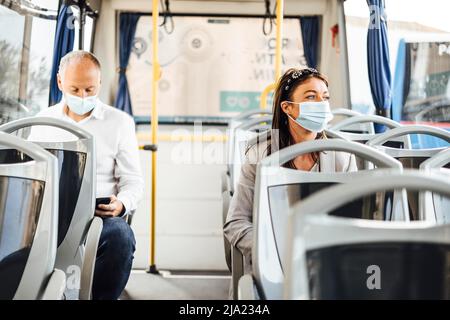 Viaggiatori che indossano maschere protettive che viaggiano con autobus pubblico Foto Stock