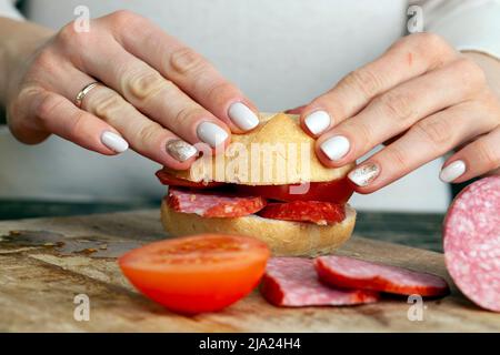 salsiccia a fette con carne, pancetta e altri prodotti alimentari durante la preparazione di sandwich, preparare sandwich a casa Foto Stock