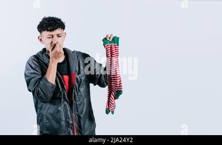 Un uomo con un calzino in mano che copre il naso, una persona che tiene un calzino stinky in mano, puzzolente calzini concetto Foto Stock