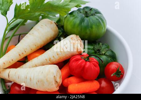 Cucina sveva, preparazione della radice di prezzemolo (Petroselinum crispum subsp. Tuberosum) a buccia con pomodori rossi e verdi, carote, verdure invernali Foto Stock