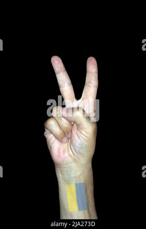 Immagine simbolica per la vittoria e la pace, mano maschile con un tatuaggio della bandiera Ucraina, fotografia studio con sfondo nero Foto Stock