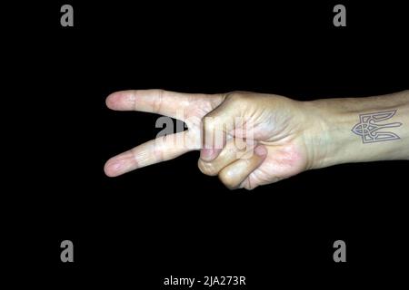 Immagine simbolo per la vittoria e la pace, mano maschio con un tatuaggio del logo dell'Ucraina, fotografia studio con sfondo nero Foto Stock