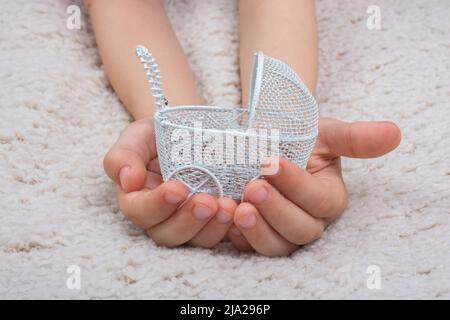 Mani piccole che tengono il passeggino del bambino su sfondo bianco Foto Stock