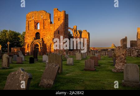 Gli ultimi raggi del sole serale illuminano le rovine del Priorato di Lindisfarne con il Castello in lontananza, Holy Island, Northumberland, Inghilterra, Regno Unito Foto Stock