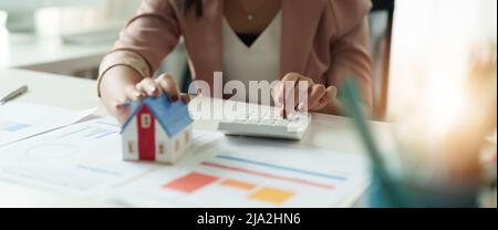 Businesswoman che lavora facendo le finanze e il costo di calcolo dell'investimento di bene immobile mentre sta firmando al contratto, approvazione di prestito ipotecario di concetto Foto Stock