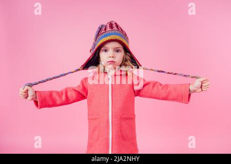 Ritratto di piccola ragazza felice affascinante che indossa divertente cappello lavorato a maglia da Himalayas Nepal su sfondo rosa in studio. Moda autunno inverno stagione vendita Foto Stock