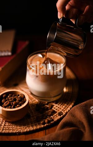 Un barista versa un caffè freddo o un caffè scuro in un bicchiere di latte fresco ghiacciato. Immagine del caffè su sfondo scuro. Bevande rinfrescanti Foto Stock