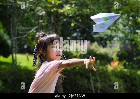 Bambini felici che giocano con l'aeroplano di carta nel giardino estivo. Carina bambina gettando aerei di carta nel parco. Concetto di infanzia felice. Foto Stock