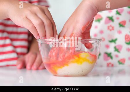 I bambini aggiungono la colorazione del cibo al sale in una ciotola di vetro e la mescolano con le loro mani. Sale colorato art. Fai da te attività di gioco e apprendimento per i bambini. Foto Stock