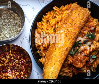 Focalizzazione selettiva della pasta Fusilli Arrabiata e una fetta di pane servita su una teglia di ferro nera. Foto Stock