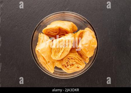 Diversi pezzi di dolce baklava miele in una ciotola di vetro su una pietra ardesia, primo piano, vista dall'alto. Foto Stock