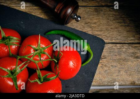 Pomodori rossi e peperoncino verde su ardesia sullo sfondo due peperoni Foto Stock
