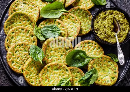 deliziose frittelle di spinaci su piatto nero con pesto di basilico su tavola di legno scuro, vista orizzontale dall'alto, primo piano Foto Stock