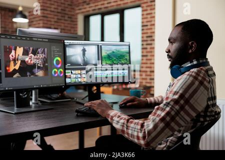 Editor professionale di riprese digitali su workstation multi monitor per migliorare la qualità visiva dei contenuti. Esperto di editing video seduto alla scrivania nello spazio di lavoro dell'ufficio, migliorando al contempo digitalmente il progetto grafico. Foto Stock