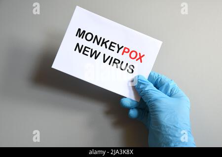 Mano del medico in guanto blu tenere carta bianca con il testo 'Monkeypox nuovo Virus'. Simbolo pandemico del virus Monkeypox. Foto Stock