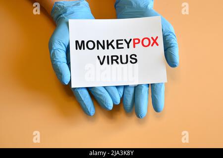 Virus Monkeypox. Le mani del medico in guanti blu tengono un libro bianco con l'iscrizione 'Monkeypox Virus'. Foto Stock