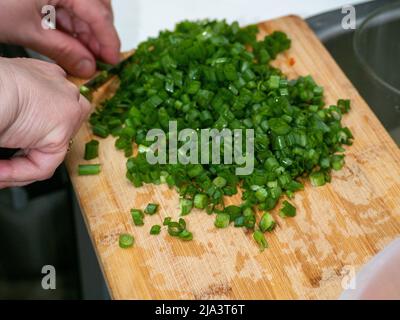 Parte di una cipolla verde trita a mano su un tagliere. Foto Stock