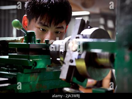 (220527) -- XINMI, 27 maggio 2022 (Xinhua) -- l'apprendista di Cheng Yucai li Jinghang regola la macchina guilloche presso il laboratorio di Cheng a Xinmi City, provincia centrale di Henan, il 24 maggio 2022. Guilloche è una tecnica decorativa in cui un disegno preciso, intricato e ripetitivo è inciso meccanicamente in un materiale attraverso la rotazione del motore. La tecnica utilizza una macchina controllata dalla delicatezza della mano dell'artigiano. Come un processo importante nel fare l'orologio e i monili superiori, l'arte ora è padronanza raramente da poca gente. Cheng Yucai, nato nel 1978, ha conosciuto guilloche nel 2013 quando Foto Stock