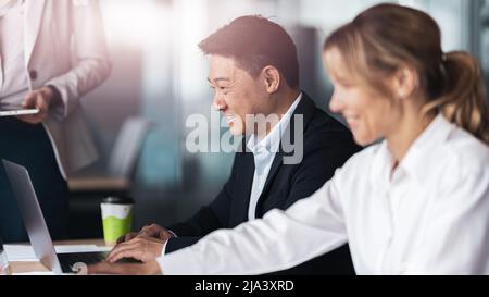 Sorridendo gli uomini d'affari nella sala riunioni discutono del progetto utilizzando un computer portatile Foto Stock