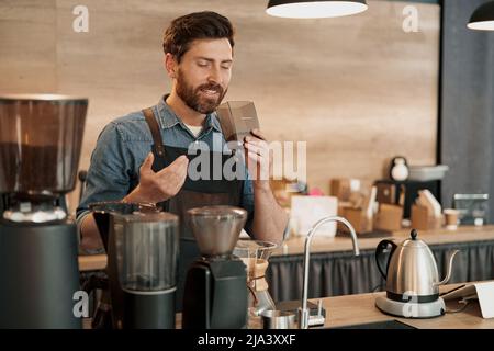 Il barista sorridente gode dell'aroma dei chicchi di caffè in caffetteria Foto Stock